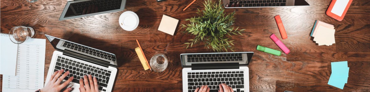 people working together around a table with laptops, coffee and notebooks